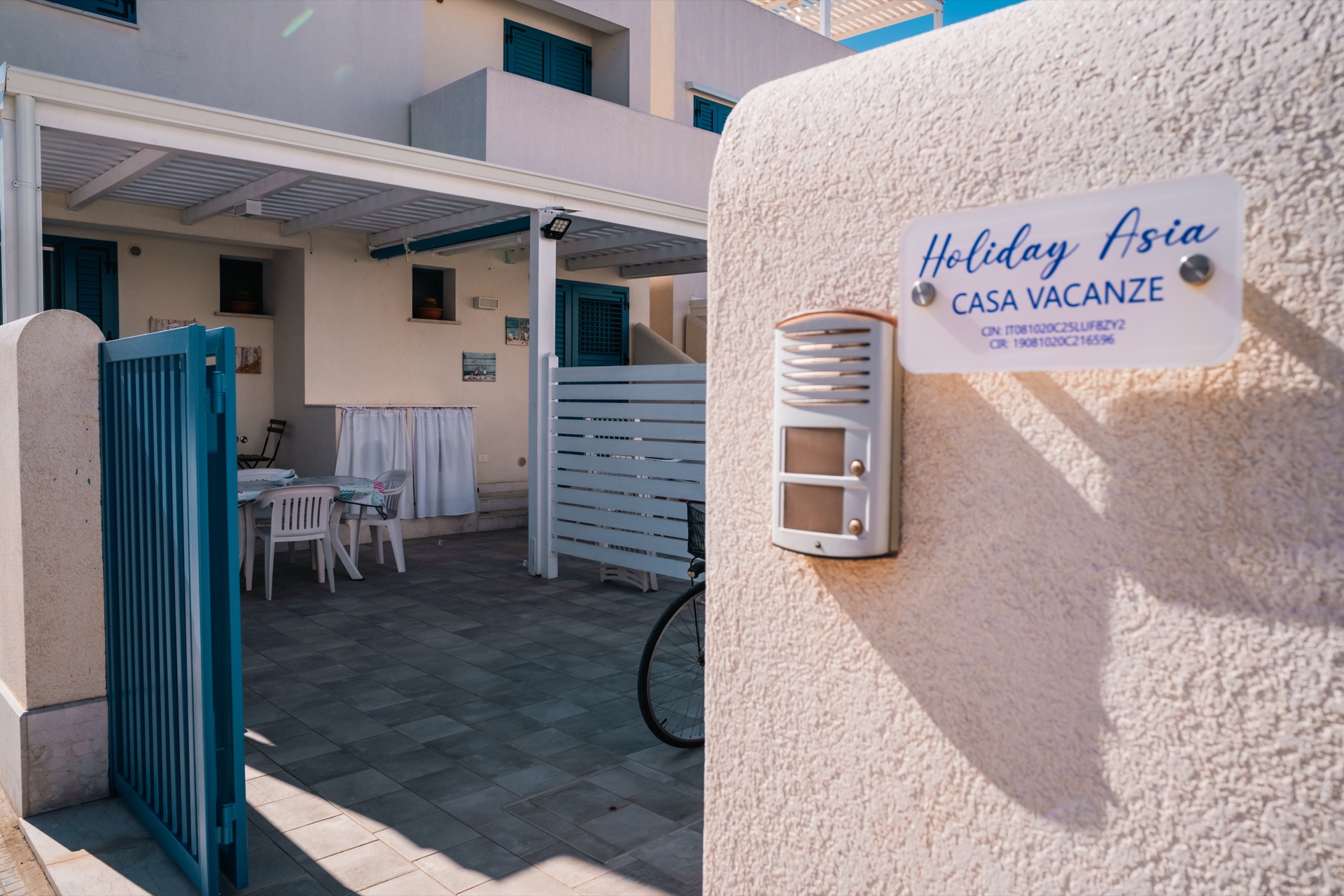 Ingresso di Holiday Asia con cancello blu, targa Casa Vacanze e veranda