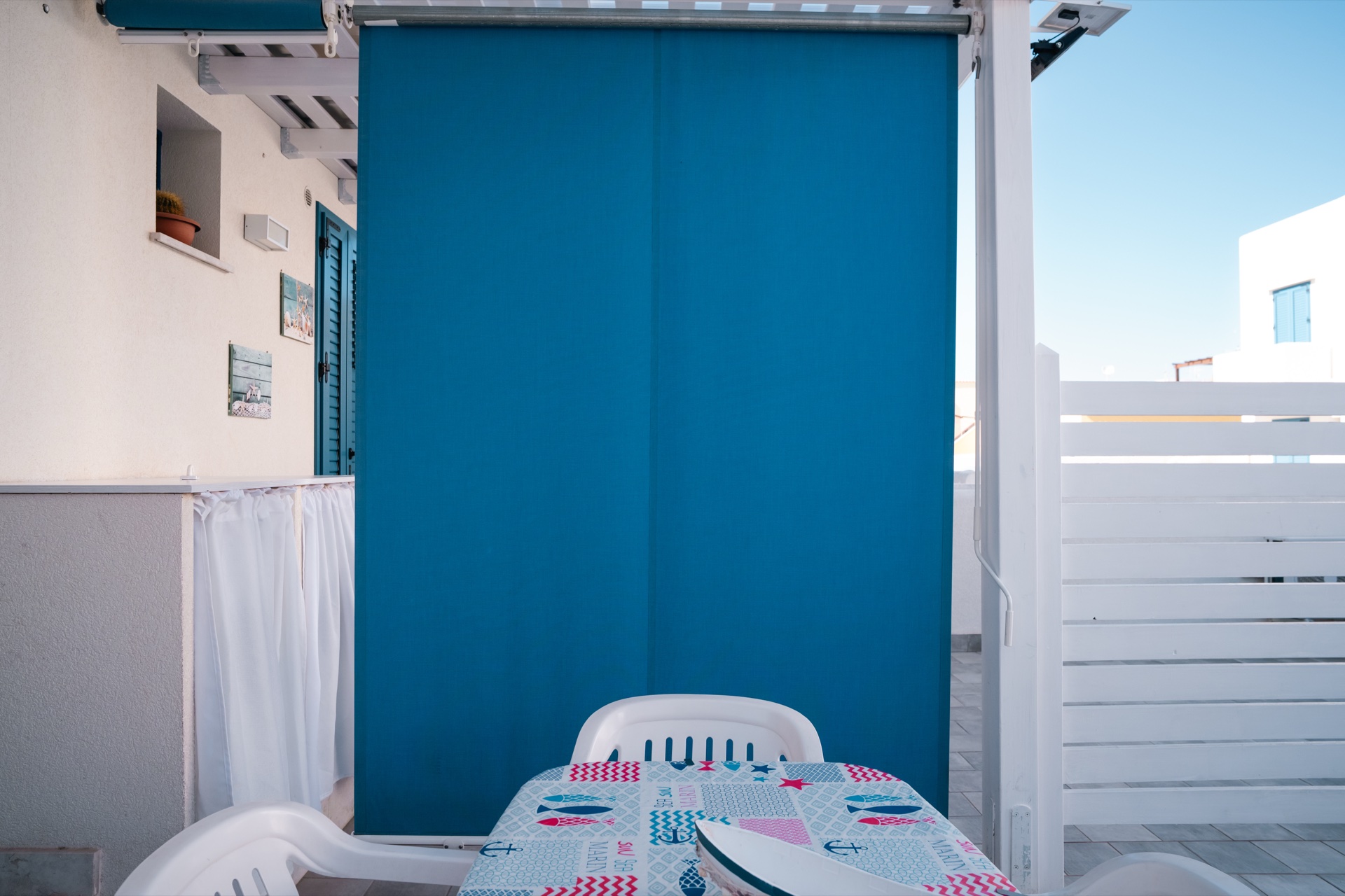 Terrazza di Casa Sofia con tenda frangisole blu, tavolo con tovaglia marinara e quadretti decorativi
