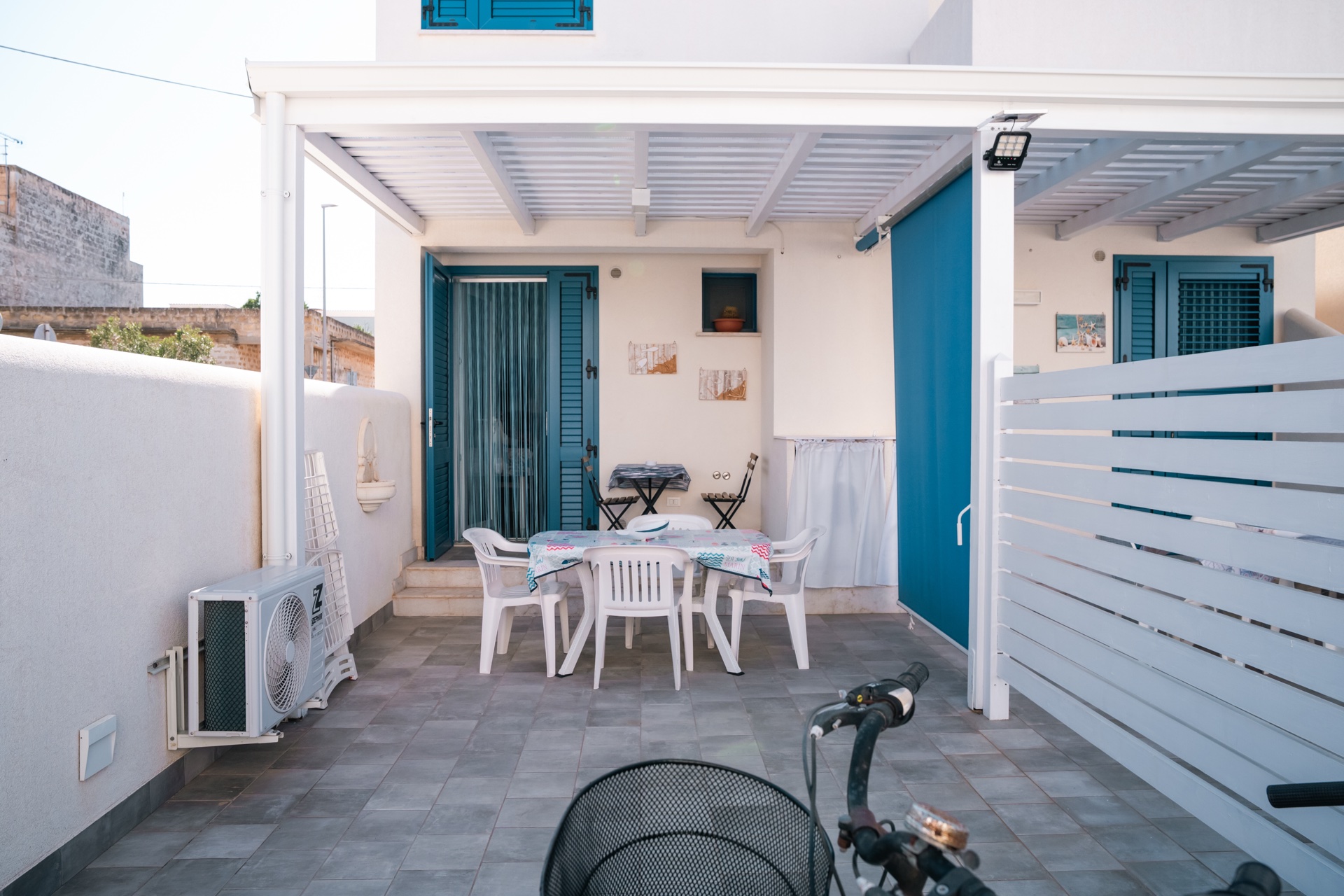 Veranda di Casa Asia con pergolato bianco, tavolo apparecchiato e bici in primo piano