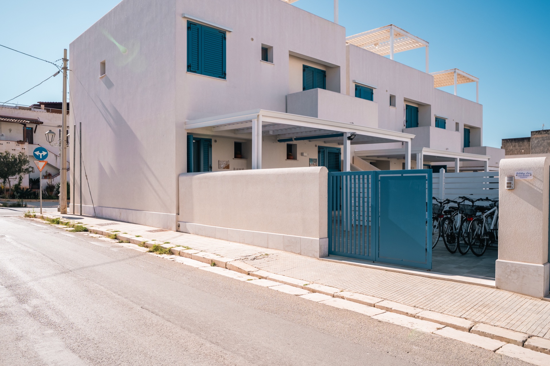 Vista esterna di Holiday Asia: facciata bianca con persiane azzurre e rastrelliera bici a lato del cancello